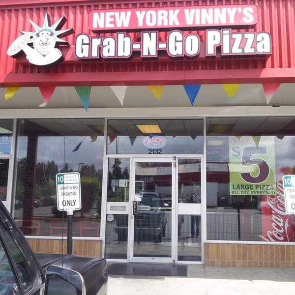 Exterior of New York Vinny's Grab-N-Go Pizza with a Statue of Liberty mascot holding a pizza.