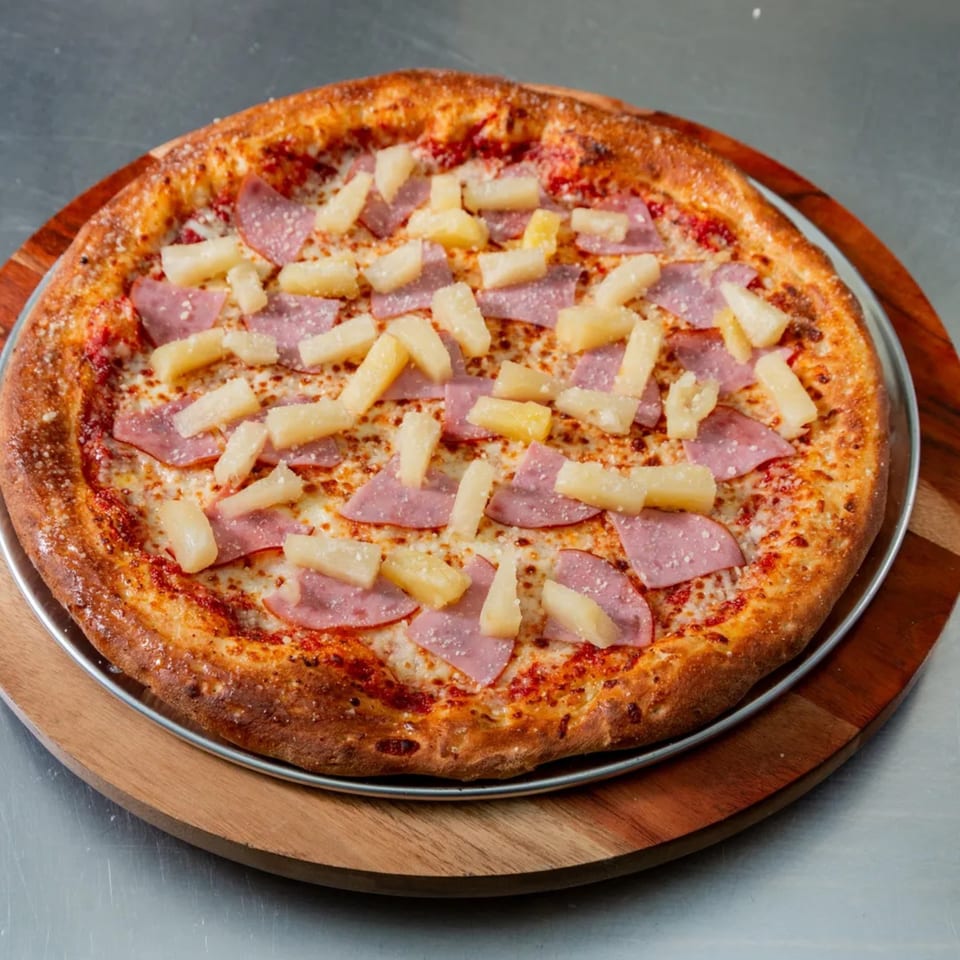 New York Vinny's Pizza Hawaiian pizza with ham and pineapple on a wooden serving board.