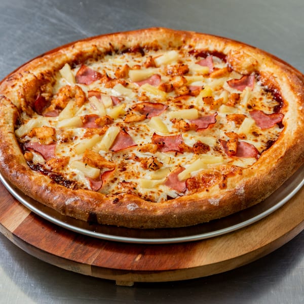 New York Vinny's Pizza with pineapple, ham, and chicken on a wooden and metal serving tray.