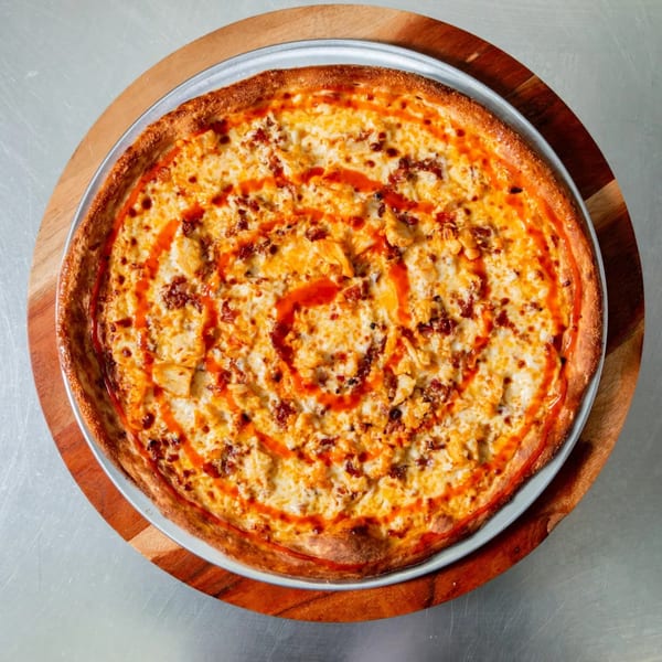 New York Vinny's Pizza's buffalo chicken pizza, drizzled with hot sauce, on a wooden board.