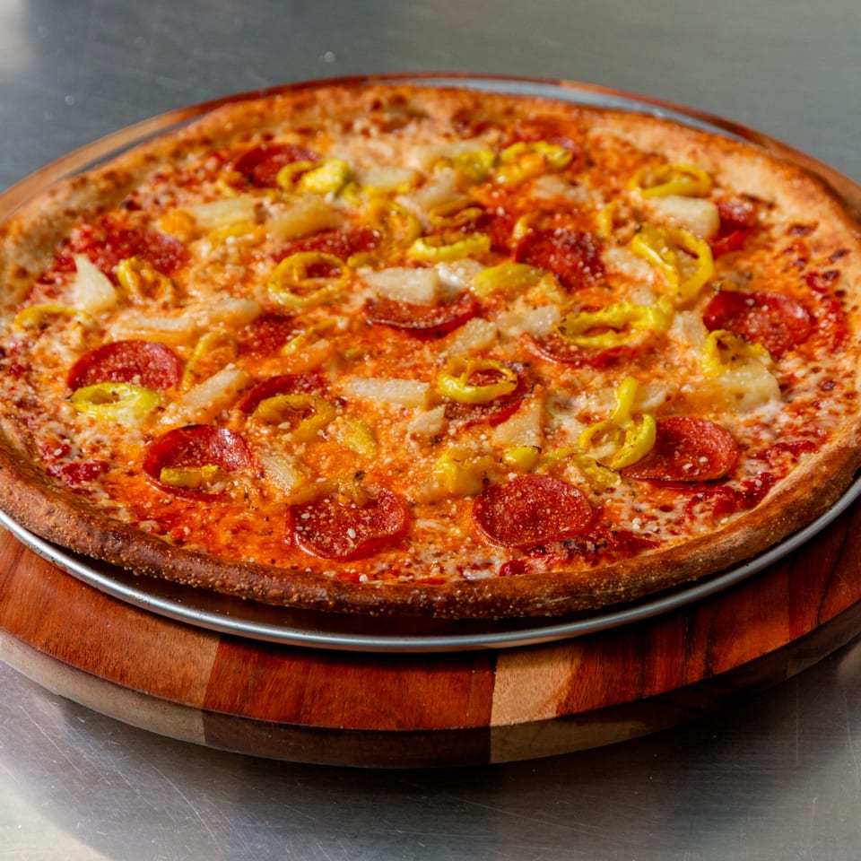 New York Vinny's Pizza with pepperoni, pineapple, and banana peppers on a wooden board.
