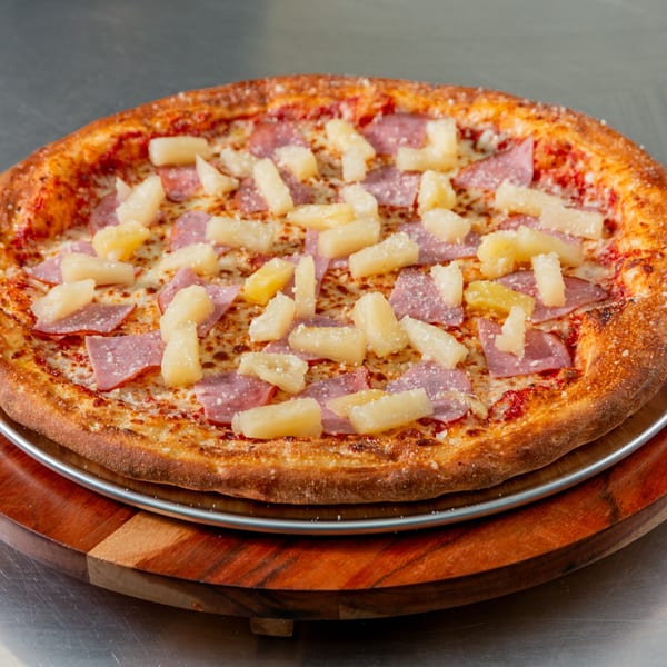 New York Vinny's Pizza with ham and pineapple toppings on a wooden and metal serving tray.